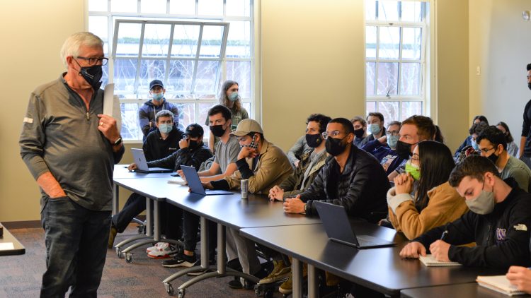 Larry Bjork standing in front of a room full of students sitting at a long table