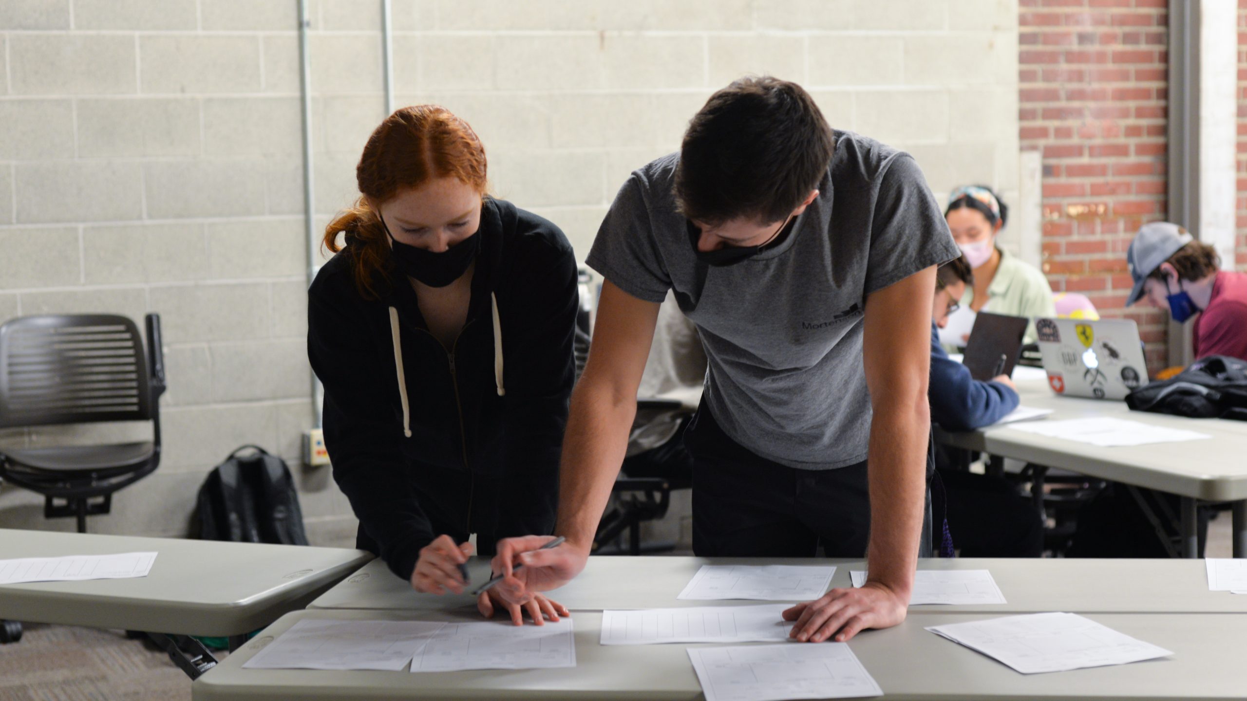 Two students stand over papers laid out on a table