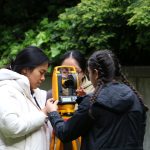 Three CM students with long brown hair learn to use survey equipment on the Gould Lawn