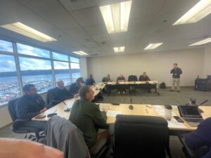 Professor Chris Lee presents in front of a group sitting at a U-shaped table.