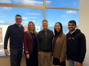 A group of 5 people standing in front of a window.