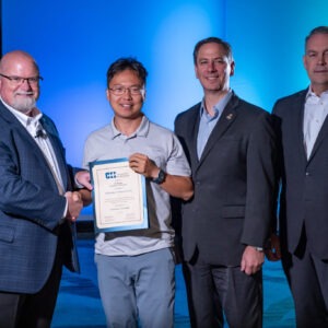 group of people standing in front of colorful background presenting award to student